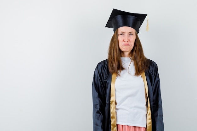 Retrato de mujer graduada mirando a la cámara mientras fruncía el ceño, curvaba los labios en ropa casual, uniforme y miraba la vista frontal ofendida