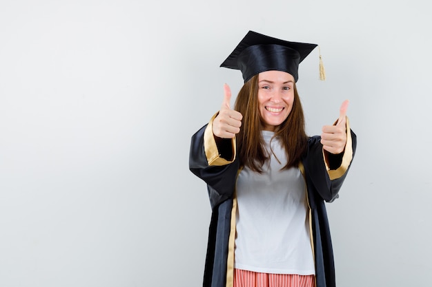 Retrato de mujer graduada mostrando doble pulgar hacia arriba en ropa casual, uniforme y mirando feliz vista frontal