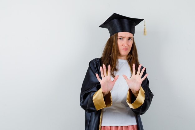 Retrato de mujer graduada mostrando gesto de parada en ropa casual, uniforme y mirando confiada vista frontal