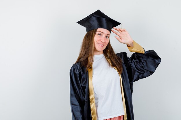 Retrato de mujer graduada mostrando gesto de saludo en uniforme, ropa casual y mirando alegre vista frontal