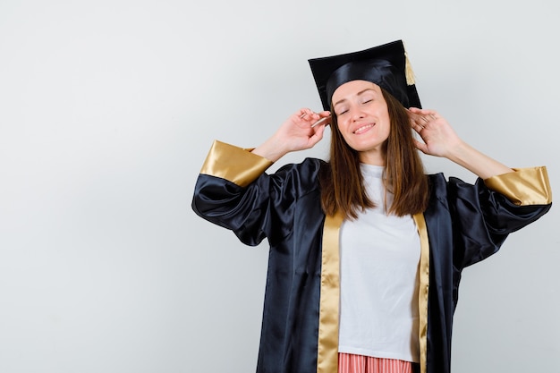 Retrato de mujer graduada posando mientras está de pie en traje académico y mirando relajado vista frontal