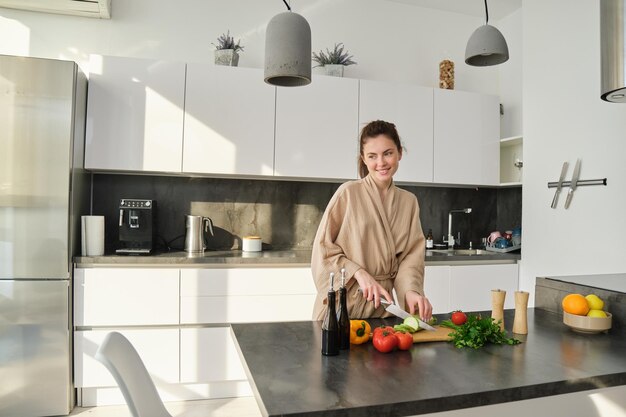 Retrato de una mujer guapa cocinando ensalada en la cocina cortando verduras y sonriendo preparando