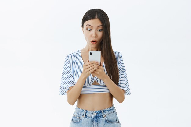 Retrato de mujer guapa divertida y sorprendida con cabello oscuro en blusa recortada a rayas diciendo wow