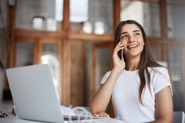 Retrato de mujer hablando por teléfono con su novio sonriendo divirtiéndose en una biblioteca pública sin guardar silencio.