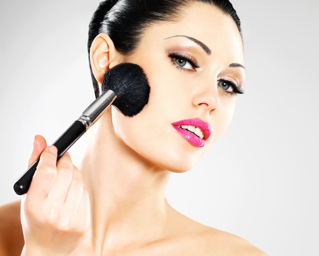 Retrato de mujer hermosa aplicando colorete en la cara con cepillo cosmético