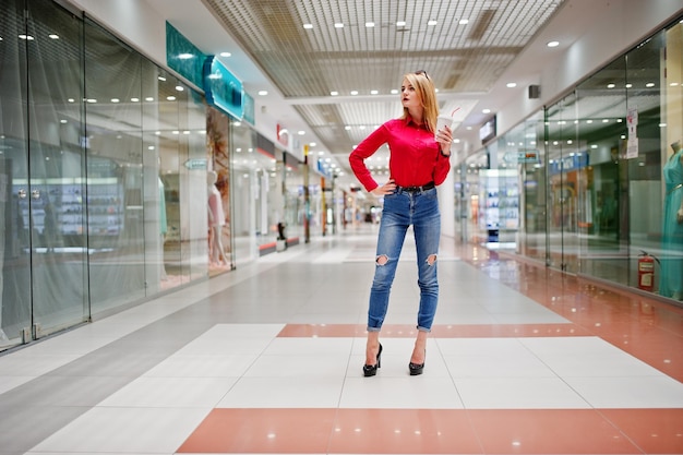 Retrato de una mujer hermosa en blusa roja y jeans sosteniendo una taza de café en un centro comercial