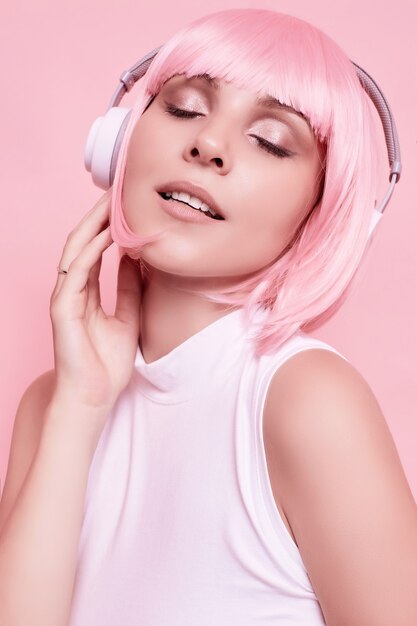 Retrato de mujer hermosa con cabello rosado disfruta de la música en auriculares