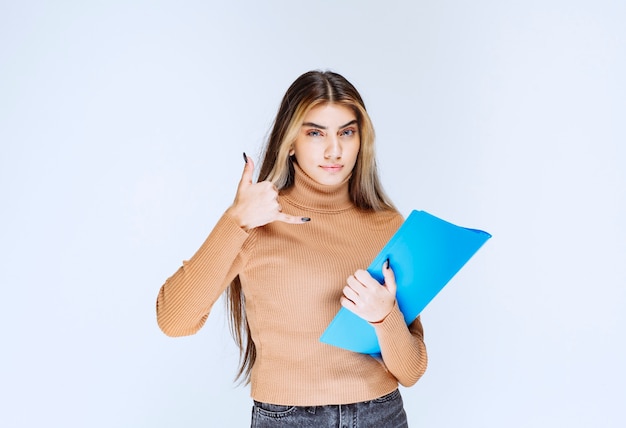 Retrato de una mujer hermosa con una carpeta de pie y haciendo una llamada telefónica.