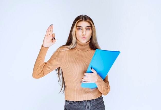 Retrato de una mujer hermosa con una carpeta de pie y mostrando gesto ok.