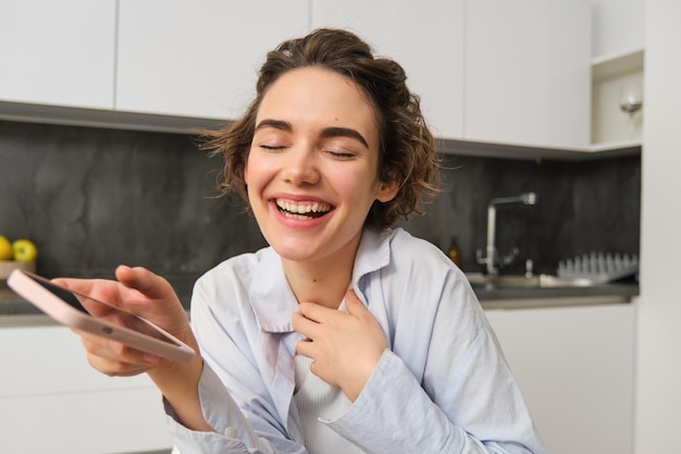 Foto gratuita retrato de una mujer hermosa en casa sosteniendo un teléfono inteligente comprando en línea desde una aplicación de teléfono móvil