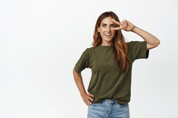 Retrato de mujer hermosa caucásica que muestra el signo v de paz en los ojos y sonriendo feliz