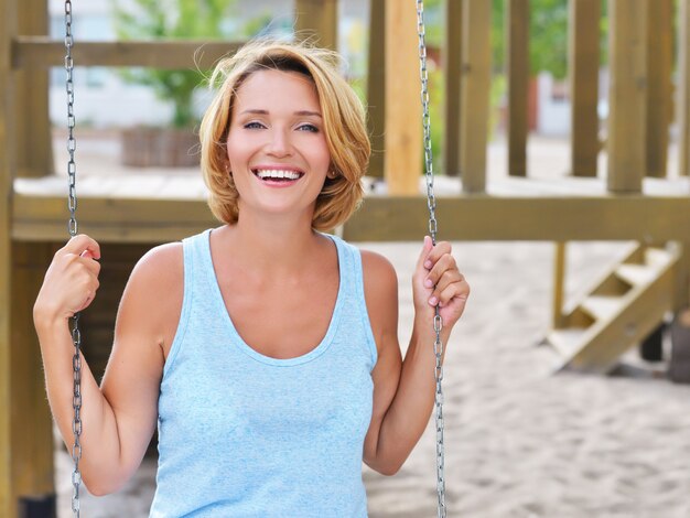 Retrato de mujer hermosa feliz divirtiéndose en un columpio en un parque de verano.