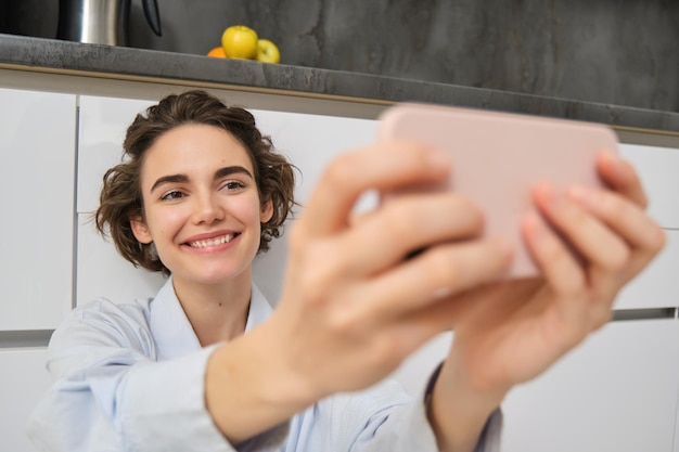 Retrato de mujer hermosa feliz toma selfie en teléfono inteligente extiende su mano con teléfono móvil y
