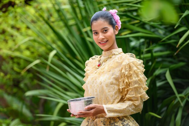 Retrato de una mujer hermosa en el festival Songkran con traje tradicional tailandés en el templo sosteniendo un tazón de agua y sonríe la cultura de Tailandia con el festival del agua