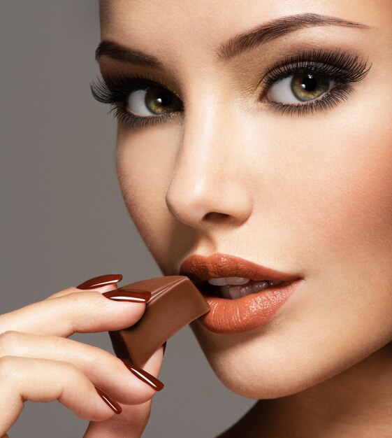 Retrato de mujer hermosa glamour sostiene y come dulces de chocolate.