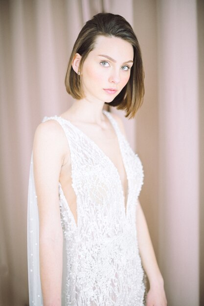 Retrato de mujer hermosa en la habitación de pie y mirando con vestido blanco largo