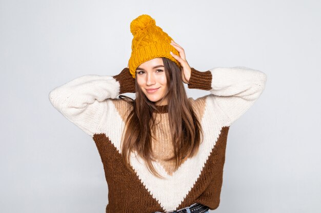Retrato de mujer hermosa invierno. Niña sonriente vistiendo ropa de abrigo divirtiéndose sombrero y suéter aislado en la pared blanca