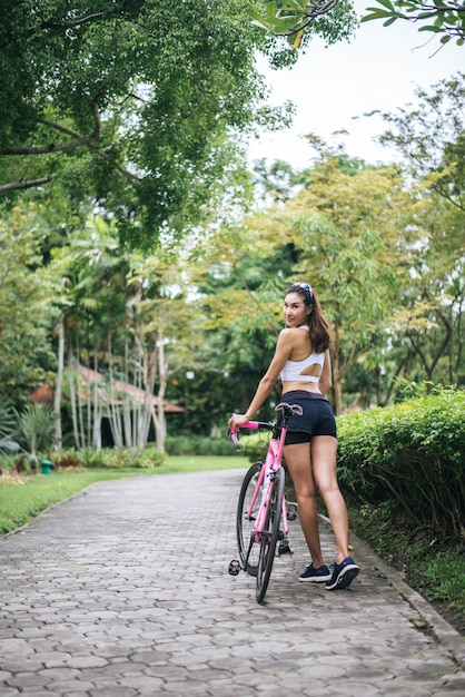Retrato de la mujer hermosa joven con la bici rosada en el parque. Mujer sana y atractiva.
