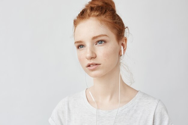 Retrato de mujer hermosa joven pelirroja escuchando música en auriculares concentrados