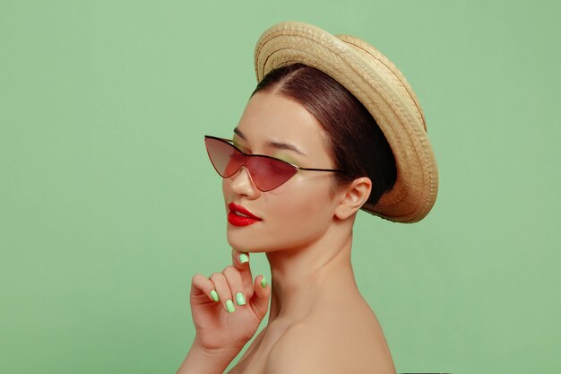 Retrato de mujer hermosa con maquillaje brillante, gafas rojas y sombrero. Hacer y peinado elegante y de moda. Colores de verano. Posando.