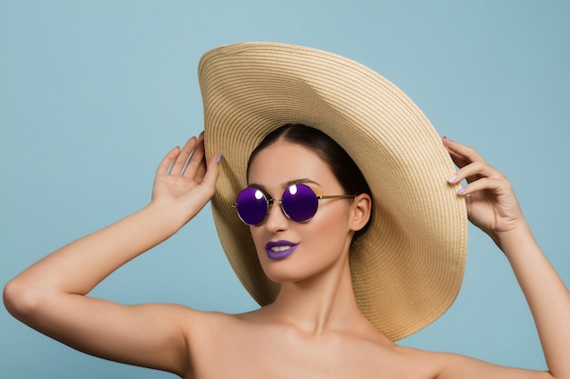 Retrato de mujer hermosa con maquillaje brillante, sombrero y gafas de sol. Hacer y peinado elegante y de moda.