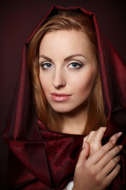 Retrato de mujer hermosa con maquillaje de noche. Modelo posando en estudio con textil rojo en la cabeza