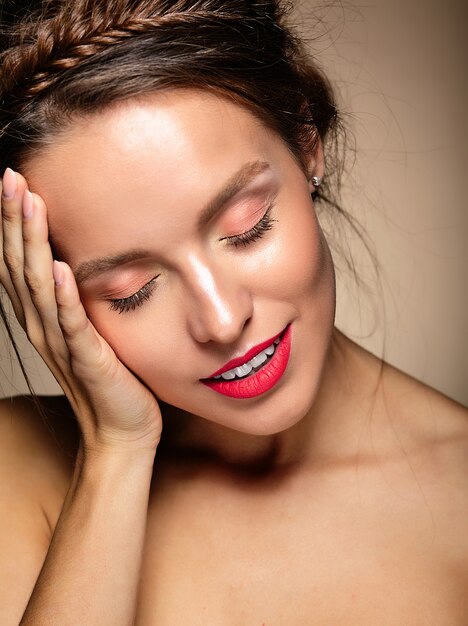 Retrato de mujer hermosa modelo con maquillaje diario fresco y labios rojos tocando su cabeza