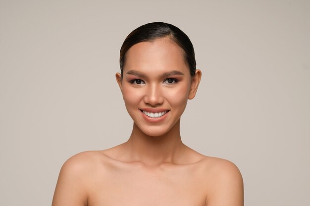 Retrato de mujer hermosa modelo con maquillaje diario fresco y sonrisas con dientes con rostro hermoso en pared gris en estudio