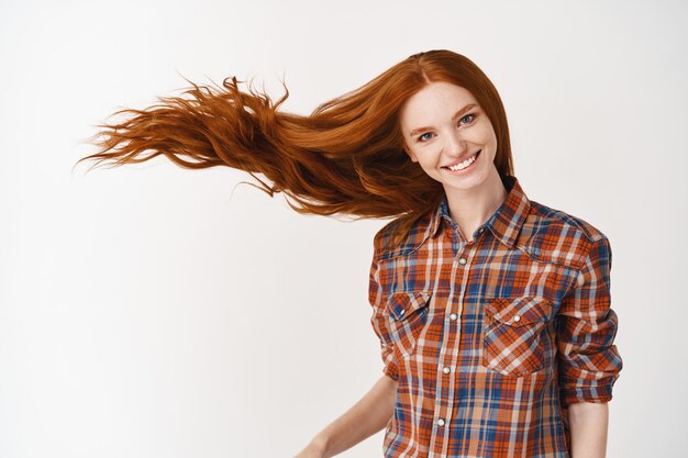 Retrato de mujer hermosa pelirroja alegre con pelo rizado volando sonriendo riendo mirando al frente sobre pared blanca