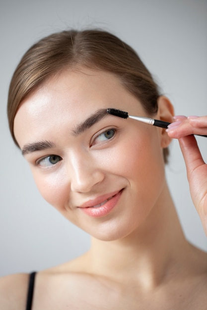 Retrato de mujer hermosa con piel clara cepillándose las cejas