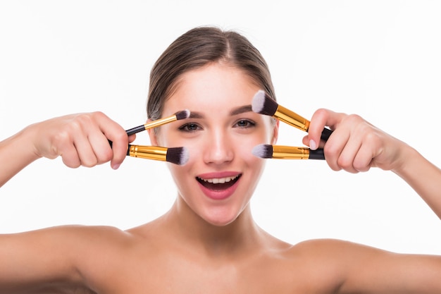 Retrato de mujer hermosa con pinceles de maquillaje cerca de cara atractiva sobre pared blanca