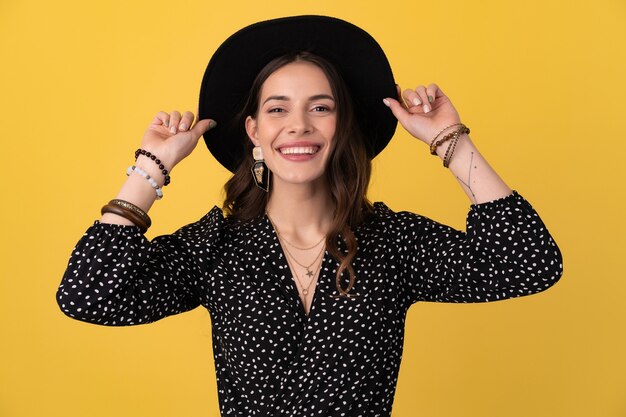 Retrato de mujer hermosa posando aislado en amarillo con vestido negro punteado y sombrero negro