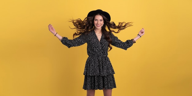 Retrato de mujer hermosa posando aislado en amarillo con vestido negro punteado y sombrero negro