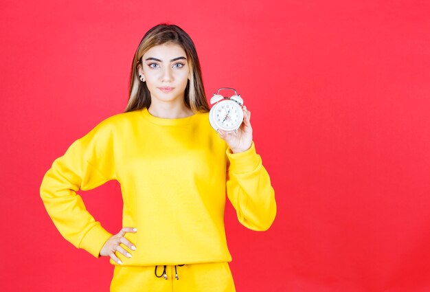 Retrato de mujer hermosa que muestra un pequeño reloj en la pared roja