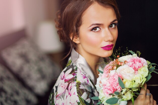 Retrato de mujer hermosa recién casada iniciar la preparación del día de la boda en albornoz floral