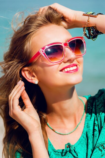 Retrato de mujer hermosa rubia bastante joven en gafas de sol frescas posando en la soleada playa tropical