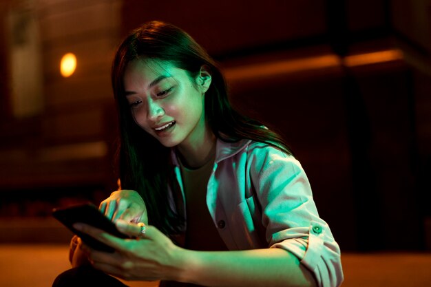 Retrato de mujer hermosa con smartphone por la noche en las luces de la ciudad