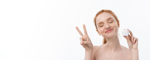 Retrato de mujer hermosa sonriendo mientras toma un poco de crema facial aislado sobre fondo blanco con