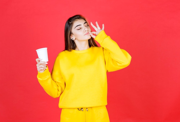 Retrato de mujer hermosa sosteniendo una taza de té de plástico y dando el signo de ok