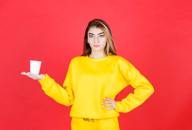 Retrato de mujer hermosa sosteniendo una taza de té de plástico en la pared roja