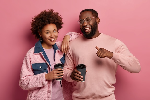 Retrato de una mujer y un hombre felices y amistosos beben café juntos, de pie cerca el uno del otro, el hombre contento se señala a sí mismo, se siente orgulloso