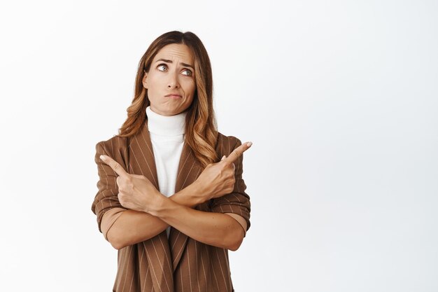 Retrato de mujer indecisa apuntando hacia los lados con cara confusa que tiene dudas mientras elige su fondo blanco