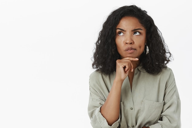 Retrato de mujer inteligente y reflexiva de aspecto serio sonriendo y frunciendo el ceño mirando hacia arriba con la mano en la barbilla