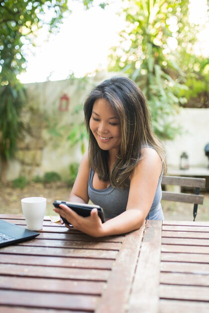 Retrato de mujer japonesa sonriente con tableta en la cafetería al aire libre. Hermosa chica con cabello castaño comprando o charlando en línea, divirtiéndose, leyendo, trabajando como autónomo. Bebiendo café