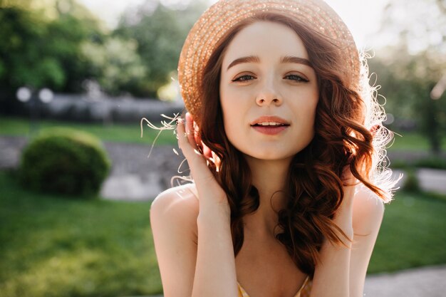 Retrato de mujer de jengibre inspirada en sombrero de verano posando en la naturaleza. Feliz modelo de mujer blanca con pelo rojo sonriendo en un día soleado.