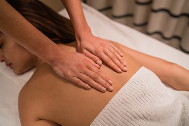 Retrato de mujer joven acostada sobre el tratamiento de mesa y recibiendo un relajante masaje de espalda en el salón de spa.