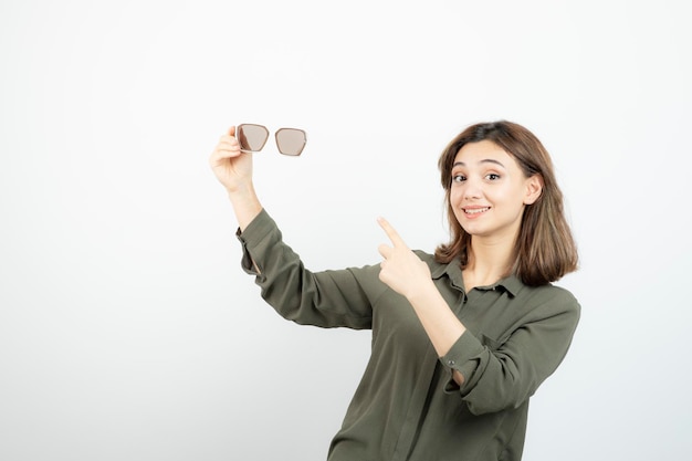 Retrato de mujer joven adorable apuntando a anteojos sobre blanco. foto de alta calidad