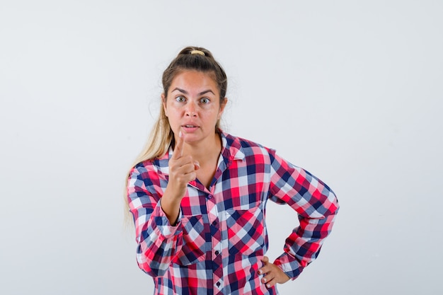 Retrato de mujer joven advirtiendo con el dedo en camisa casual y mirando enojado vista frontal