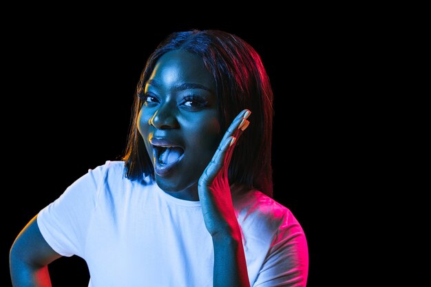 Retrato de mujer joven africana sobre fondo de estudio oscuro en neón Concepto de emociones humanas expresión facial anuncio de ventas para jóvenes