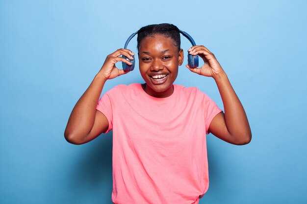 Retrato de mujer joven afroamericana despreocupada poniendo auriculares